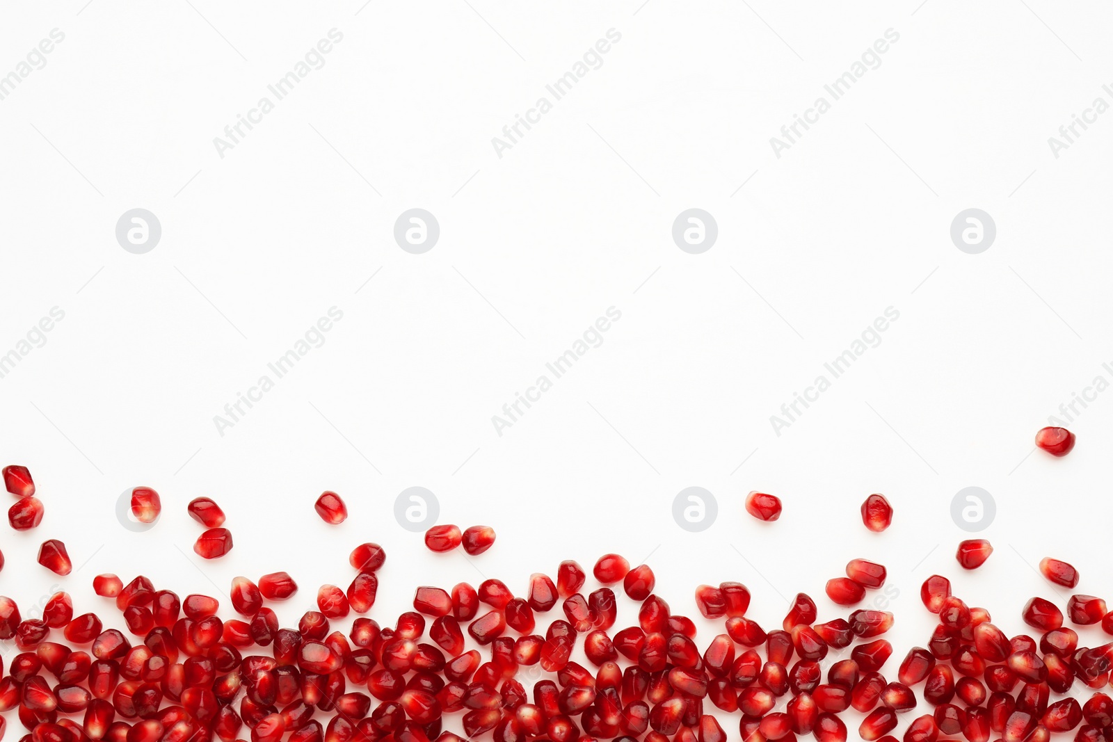 Photo of Many ripe juicy pomegranate grains on white background, flat lay. Space for text