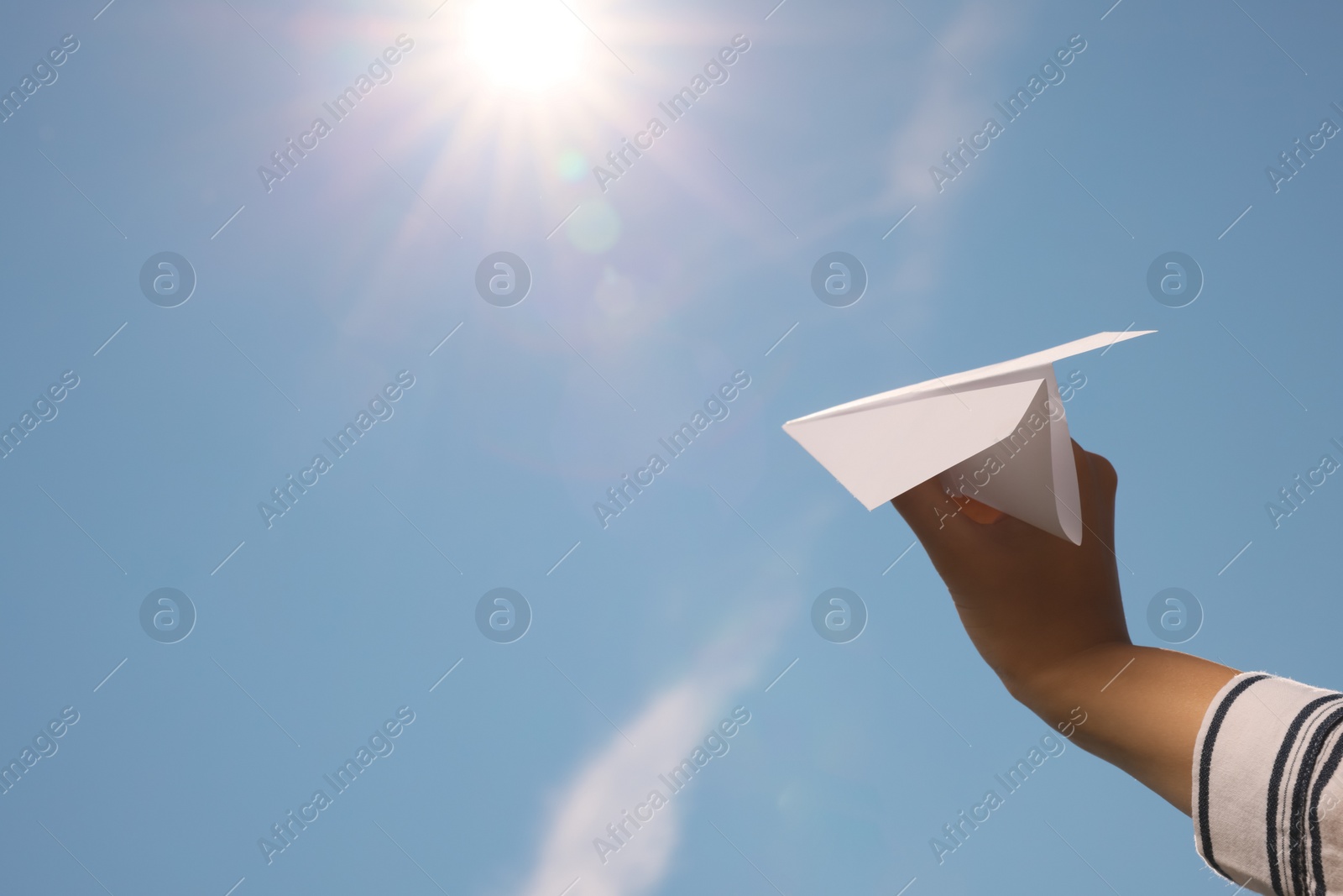 Photo of Woman holding paper plane against blue sky, closeup. Space for text
