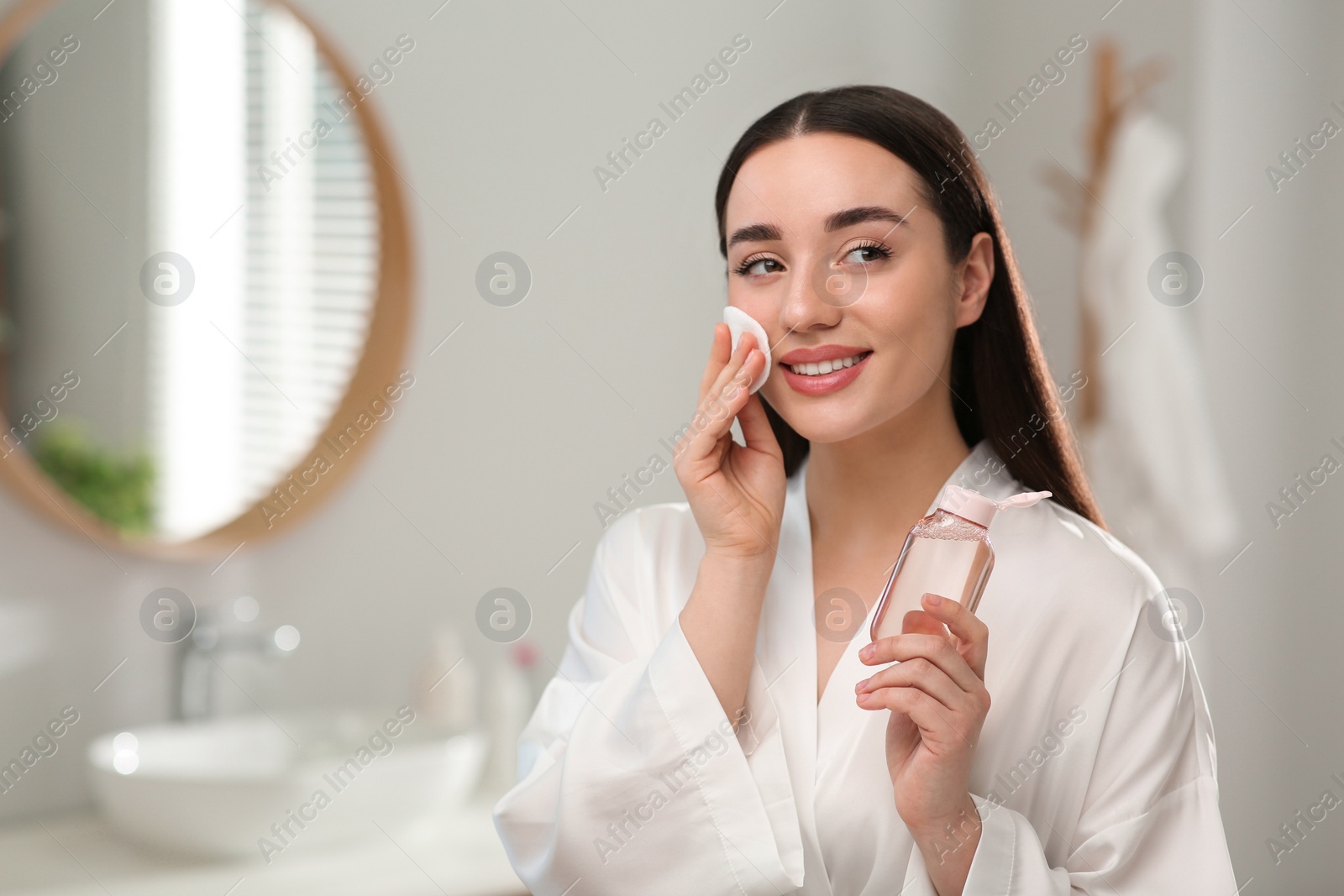 Photo of Beautiful woman removing makeup with cotton pad indoors