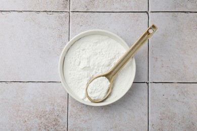 Baking powder in bowl and spoon on light tiled table, top view