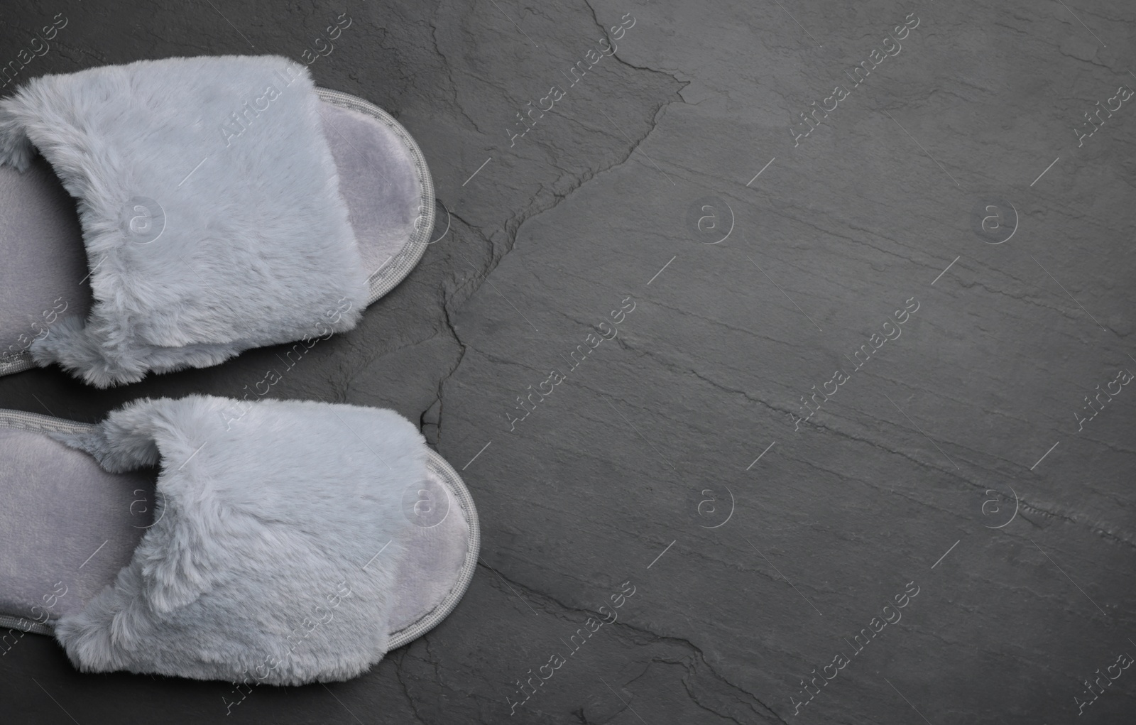 Photo of Pair of soft slippers on dark grey floor, top view, closeup. Space for text