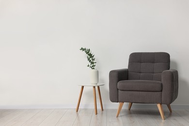 Photo of Comfortable armchair, side table and eucalyptus near white wall indoors, space for text