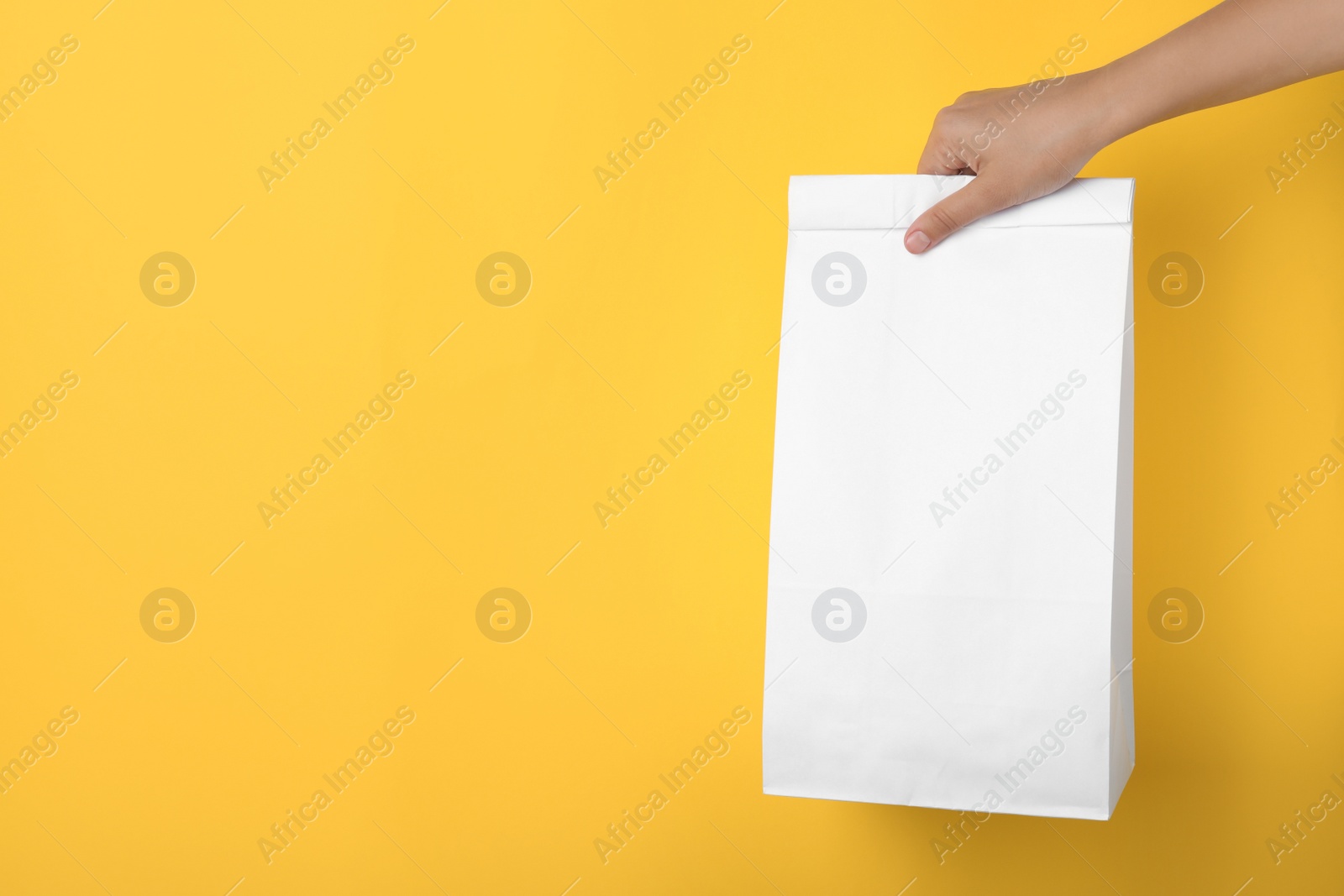 Photo of Woman holding paper bag on yellow background, closeup. Space for text