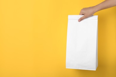 Woman holding paper bag on yellow background, closeup. Space for text