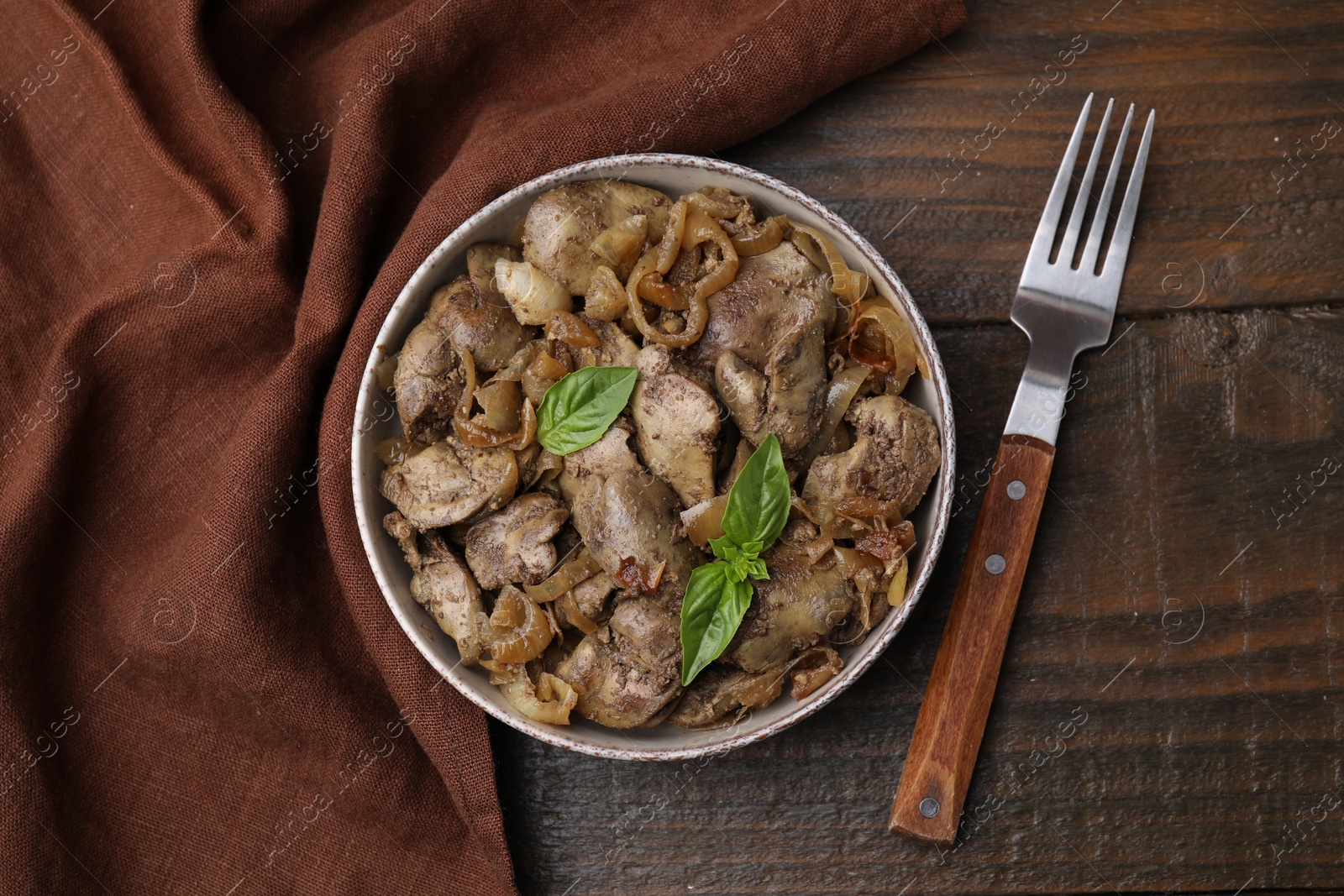 Photo of Delicious fried chicken liver with onion in bowl on wooden table, top view