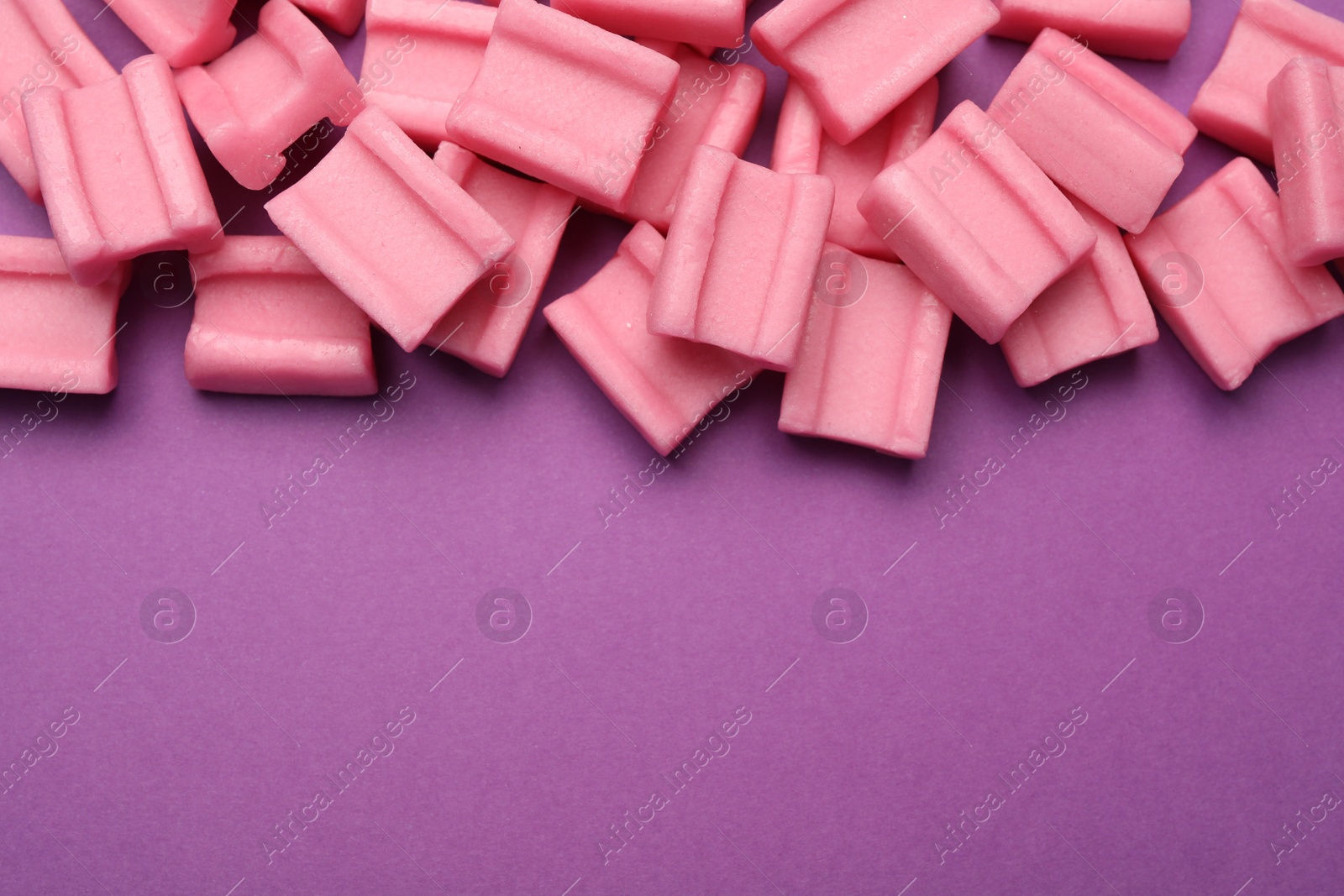 Photo of Tasty pink chewing gums on purple background, flat lay. Space for text