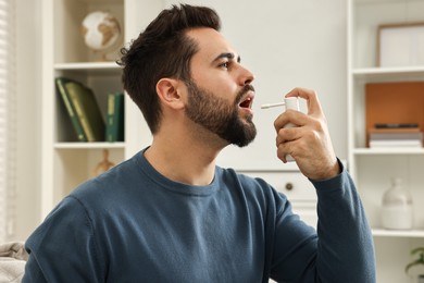 Photo of Young man using throat spray at home