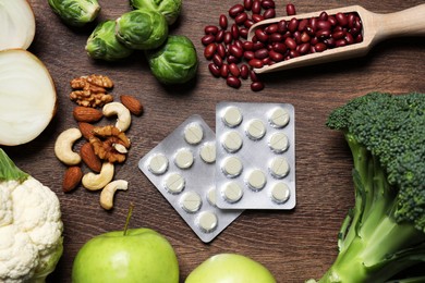 Photo of Blisters of pills and foodstuff on wooden table, flat lay. Prebiotic supplements