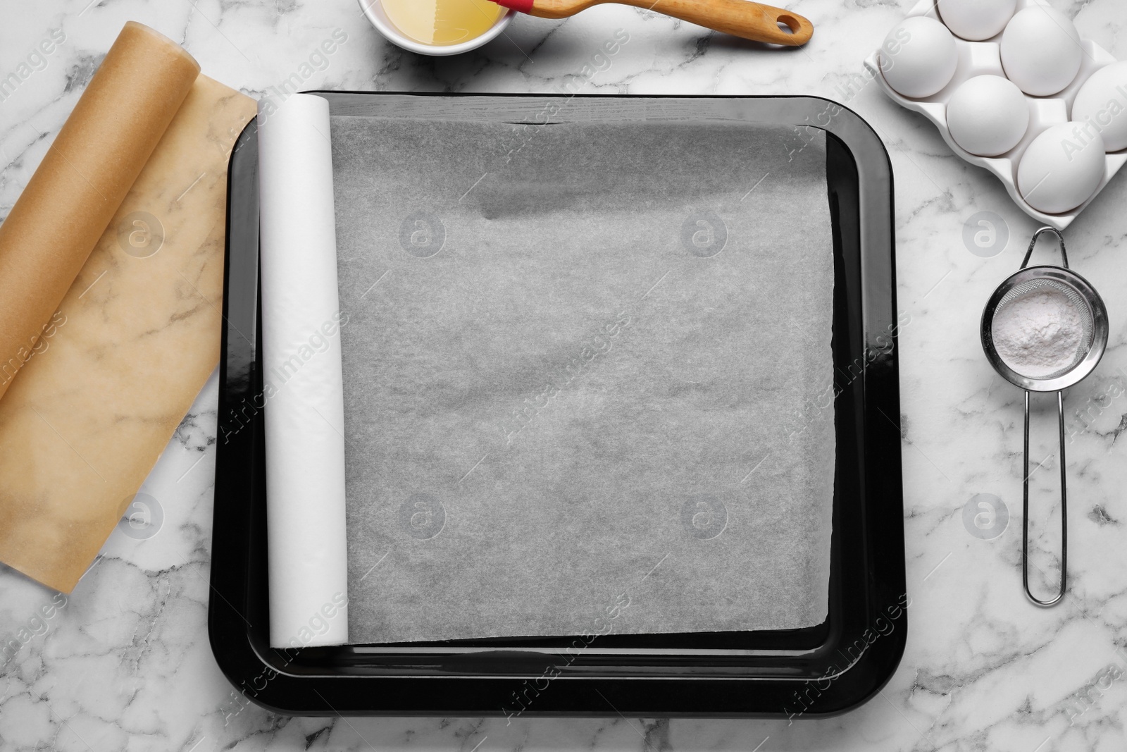 Photo of Baking pan with parchment paper, different ingredients and kitchen tools on white marble table, flat lay. Space for text