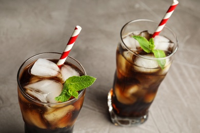 Photo of Glasses of refreshing soda drink with ice cubes and straws on grey table