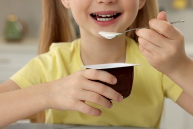Photo of Cute little girl with tasty yogurt indoors, closeup