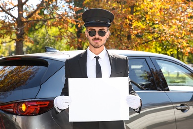 Young handsome driver with blank placard near car outdoors. Chauffeur service