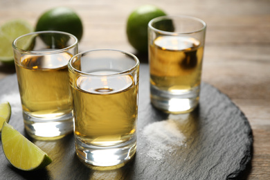 Photo of Mexican Tequila shots, lime slices and salt on wooden table