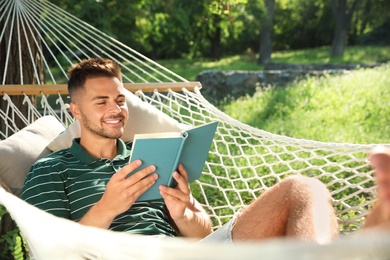 Photo of Young man reading book in comfortable hammock at green garden
