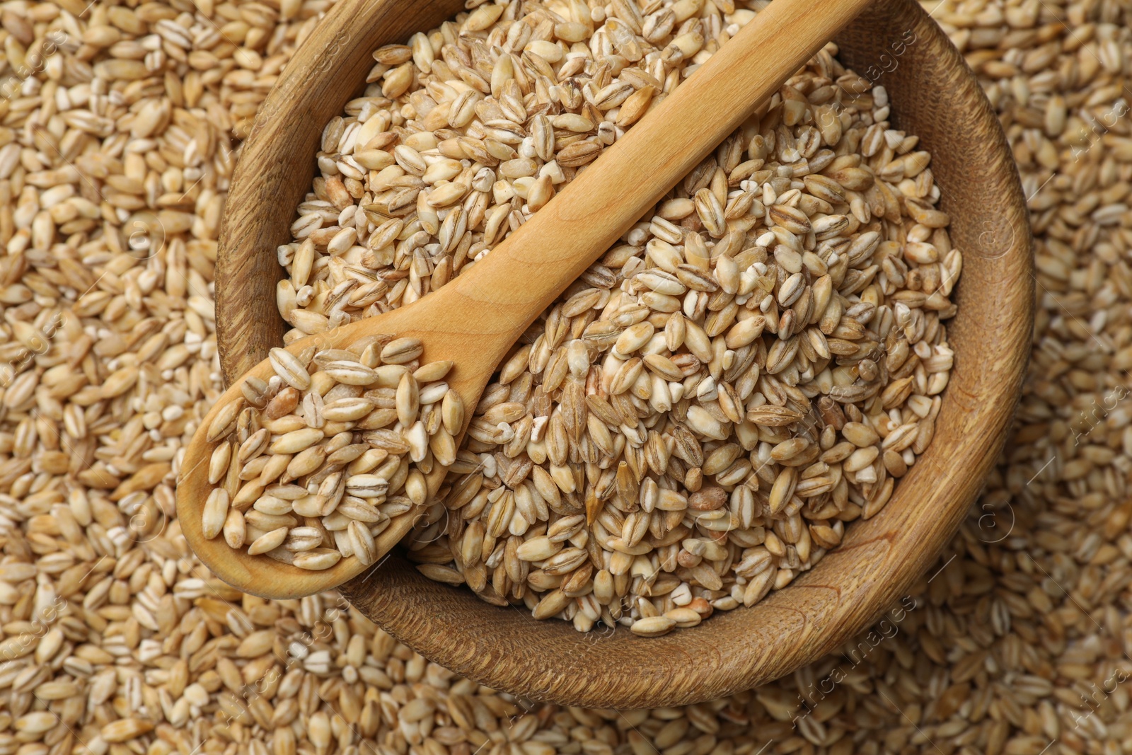 Photo of Pearl barley in bowl and spoon on dry grains, top view