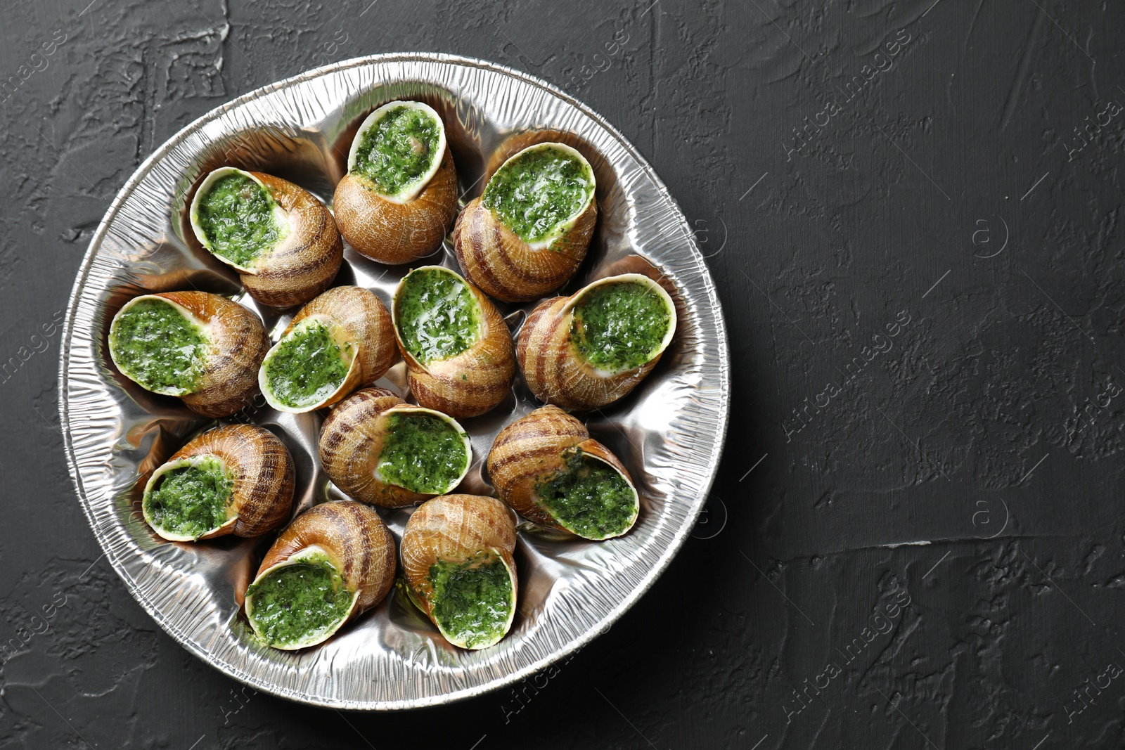 Photo of Delicious cooked snails on dark textured table, top view. Space for text