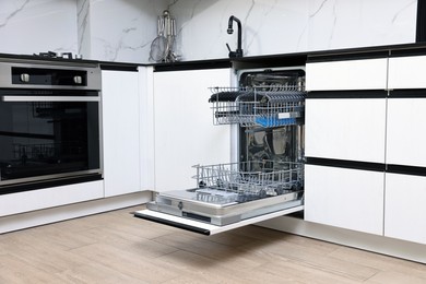 Photo of Open clean empty dishwasher in kitchen. Home appliance