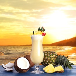 Tasty Pina Colada cocktail on blue wooden table near ocean at sunset