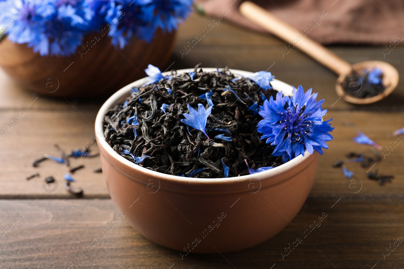 Photo of Bowl with dry tea leaves and cornflower on wooden table, closeup