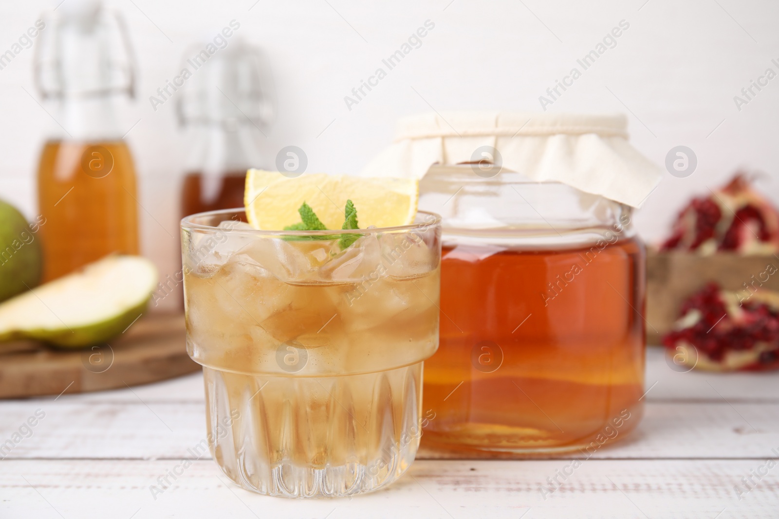 Photo of Tasty kombucha and ice cubes in glass on white wooden table, closeup