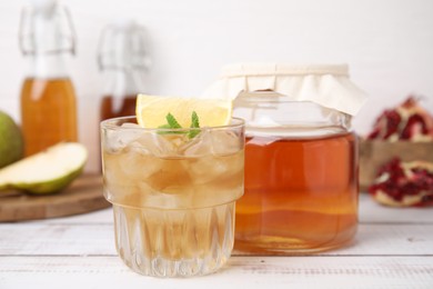 Tasty kombucha and ice cubes in glass on white wooden table, closeup