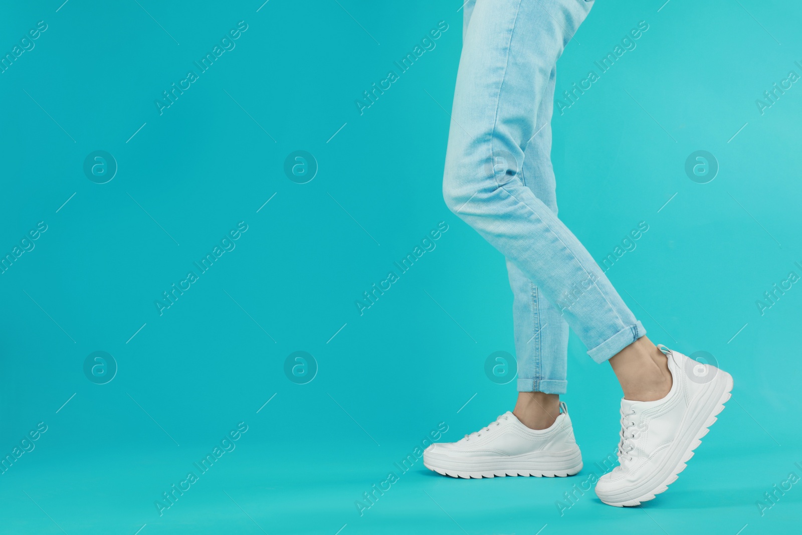 Photo of Woman in stylish sport shoes on light blue background. Space for text