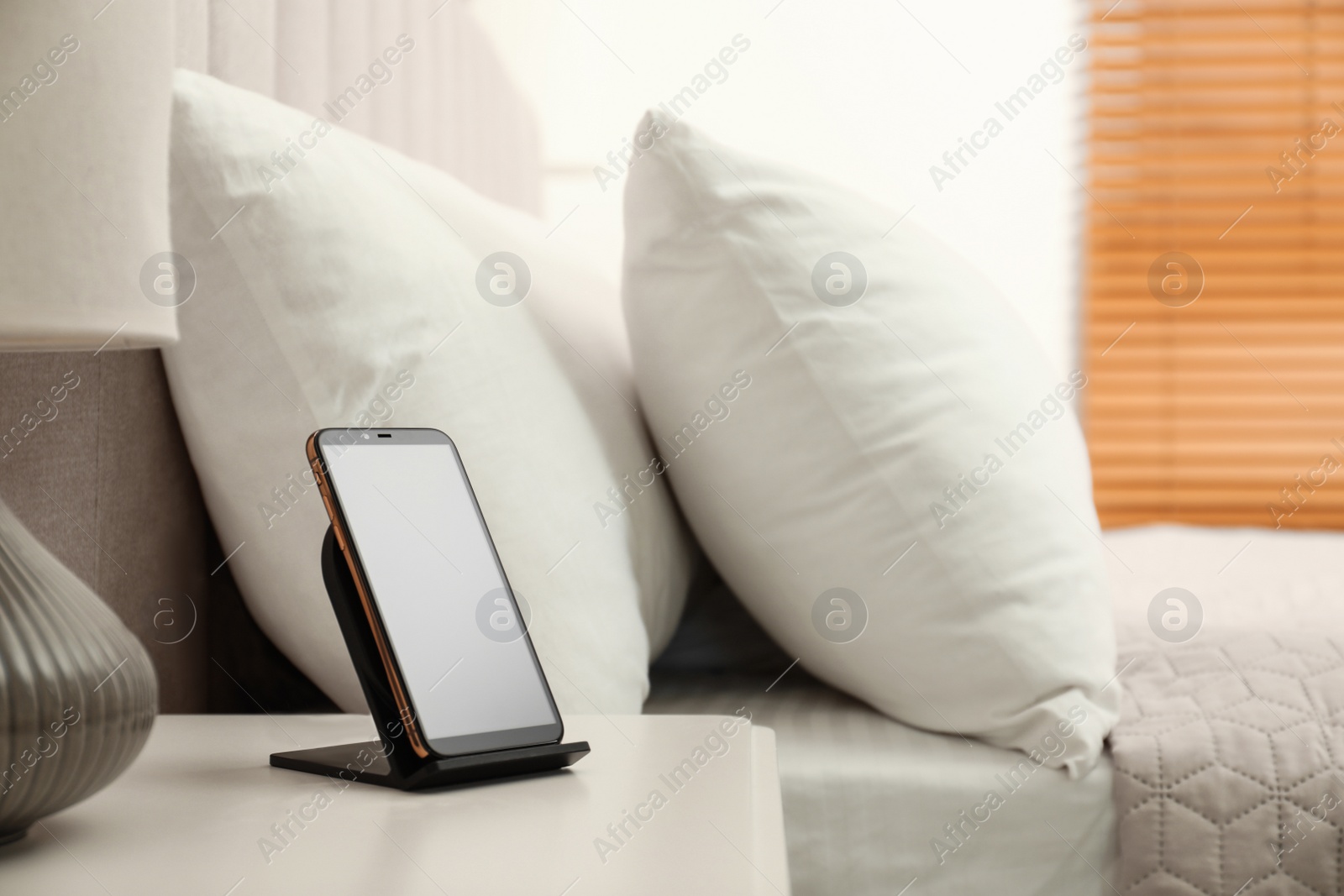 Photo of Modern mobile phone charging on wireless pad in bedroom. Space for text