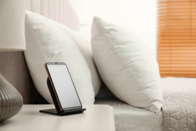 Modern mobile phone charging on wireless pad in bedroom. Space for text