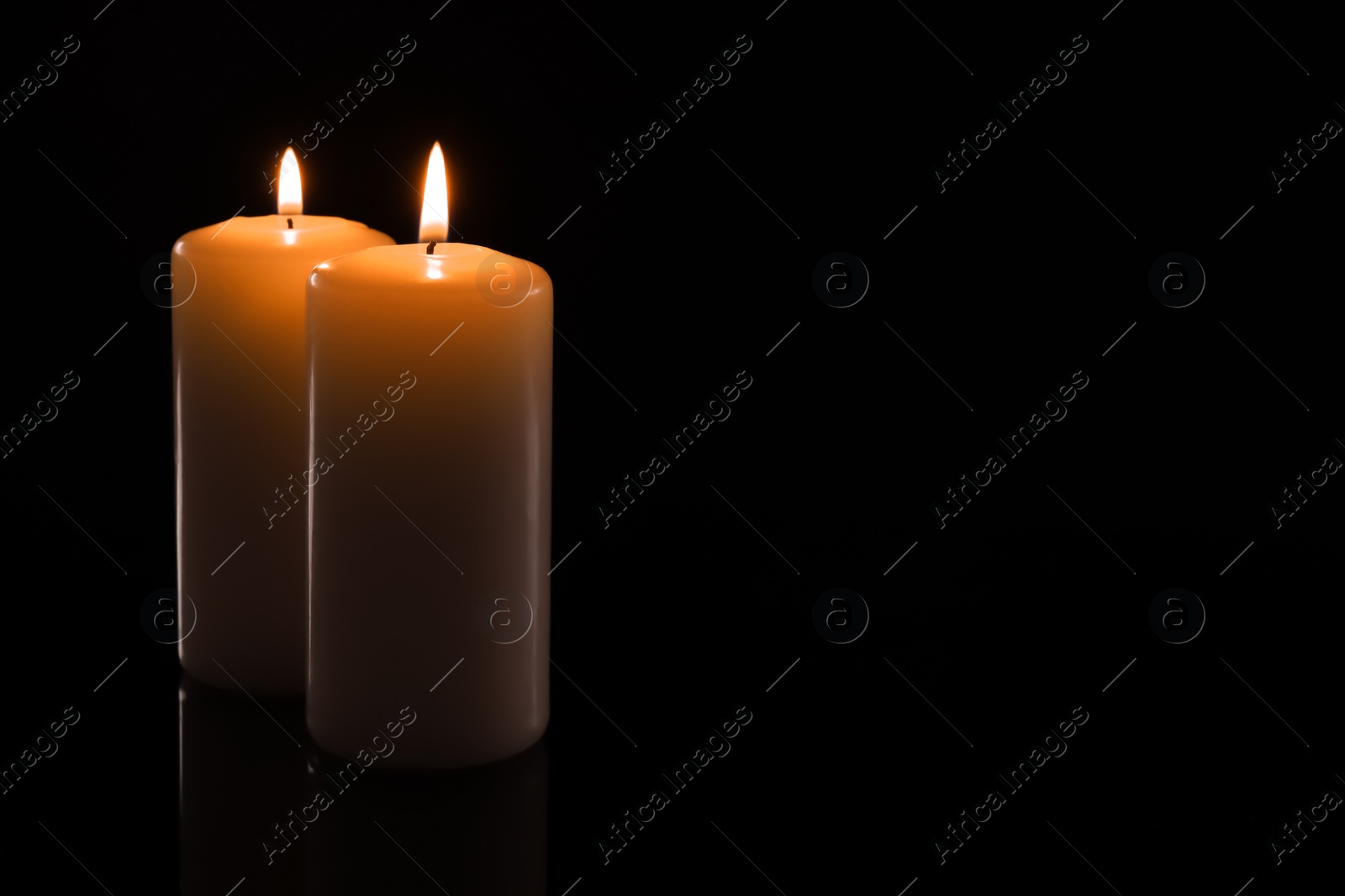 Photo of Wax candles burning on black background, closeup