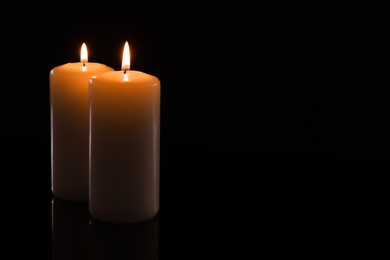 Wax candles burning on black background, closeup