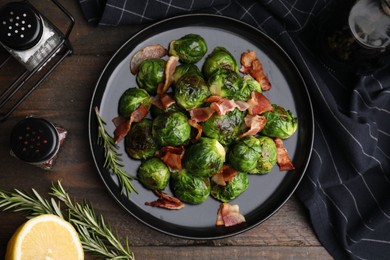 Delicious roasted Brussels sprouts, bacon, rosemary and lemon on wooden table, flat lay