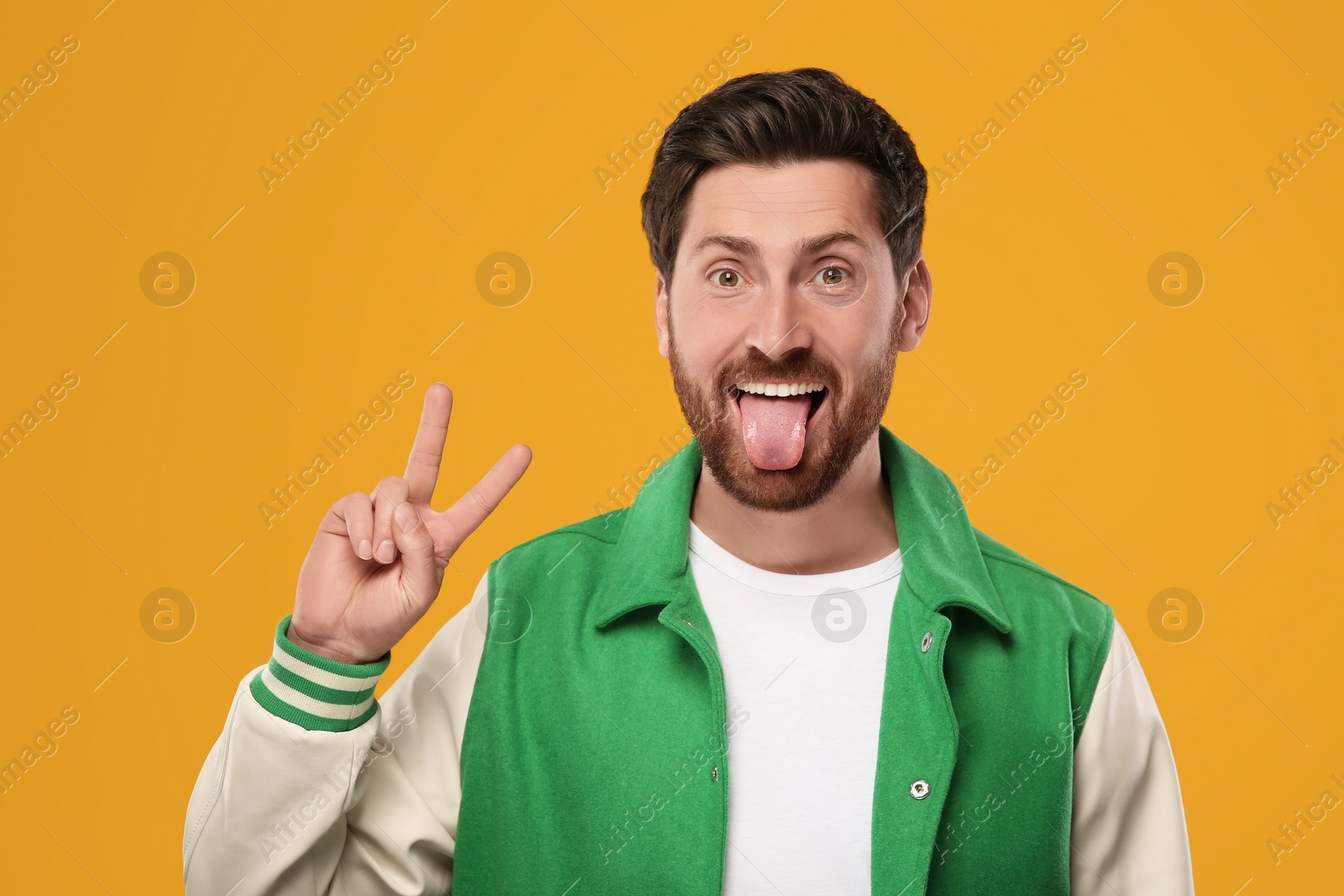 Photo of Man showing his tongue and V-sign on orange background