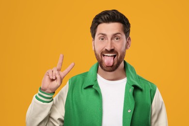 Photo of Man showing his tongue and V-sign on orange background