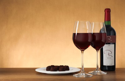 Photo of Bottle and glasses of red wine with chocolate candies on wooden table. Space for text