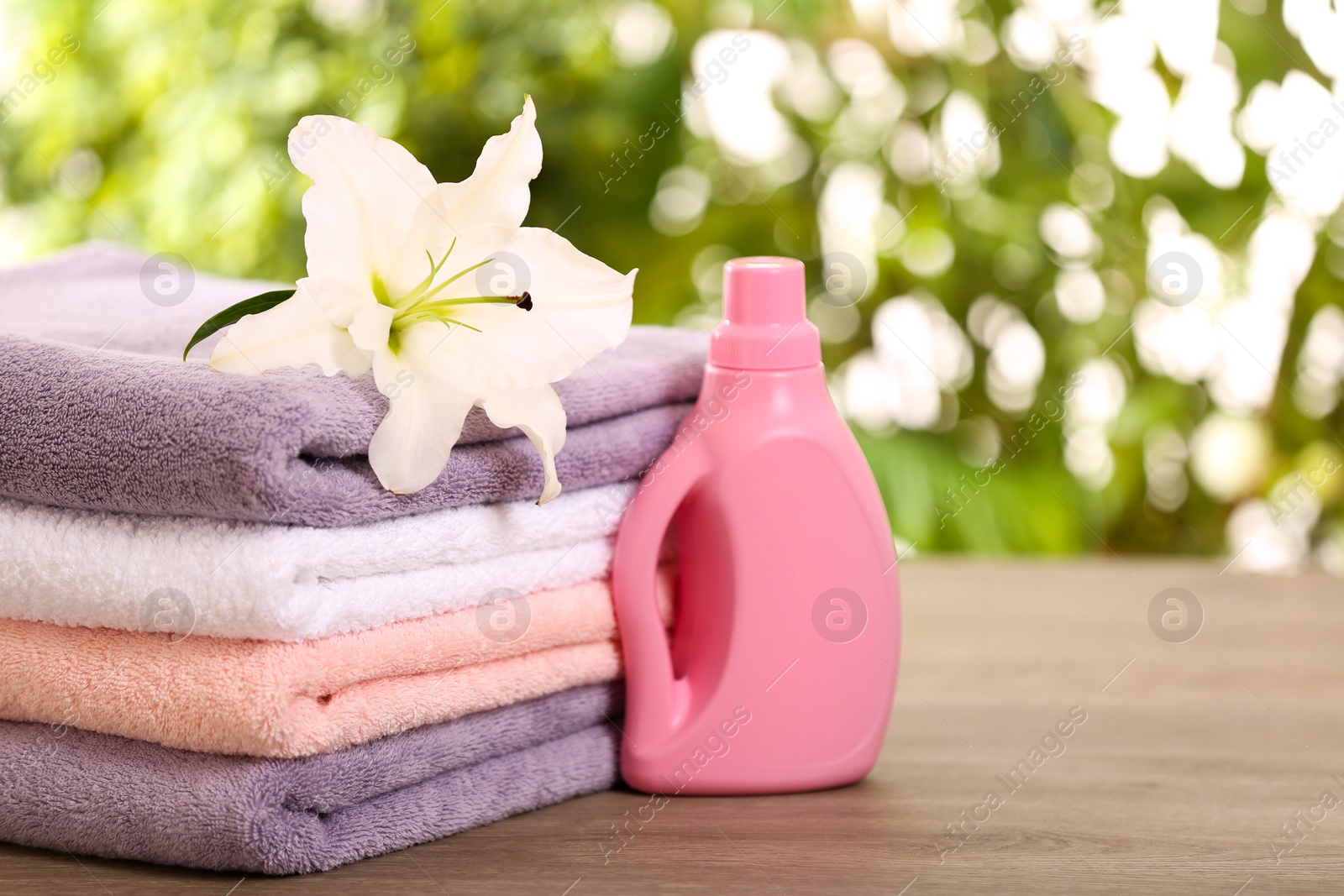 Photo of Stack of clean towels with lily and detergent on table against blurred background. Space for text