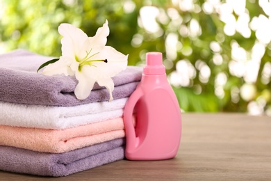 Stack of clean towels with lily and detergent on table against blurred background. Space for text