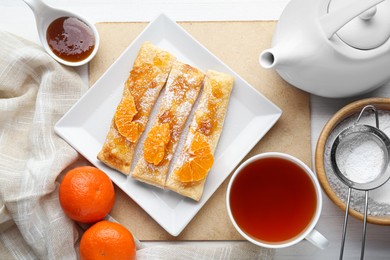 Photo of Fresh tasty puff pastry with sugar powder, jam and tangerines served on white wooden table, flat lay