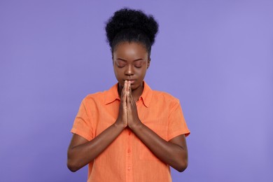 Woman with clasped hands praying to God on purple background