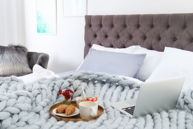 Laptop and tray with breakfast on bed in stylish room interior