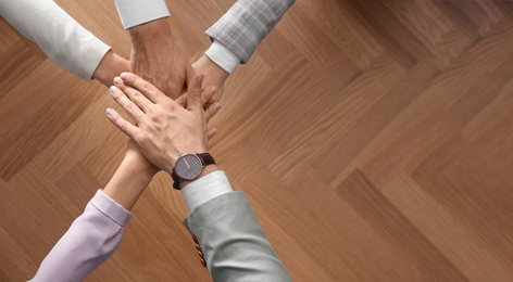 Photo of People holding hands together over wooden background, top view with space for text. Unity concept