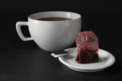 Used tea bag and cup of drink on black table