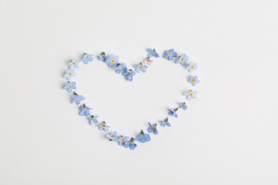 Heart made with beautiful forget-me-not flowers on white background, top view. Space for text