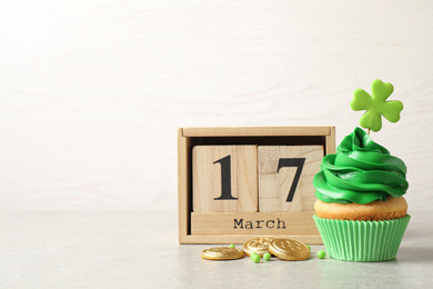 Photo of Delicious decorated cupcake, wooden block calendar and coins on light table, space for text. St. Patrick's Day celebration