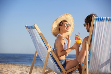 Photo of Young couple with cocktails in beach chairs at seacoast