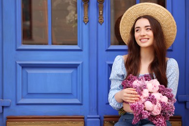 Beautiful woman with bouquet of spring flowers near blue wooden doors, space for text