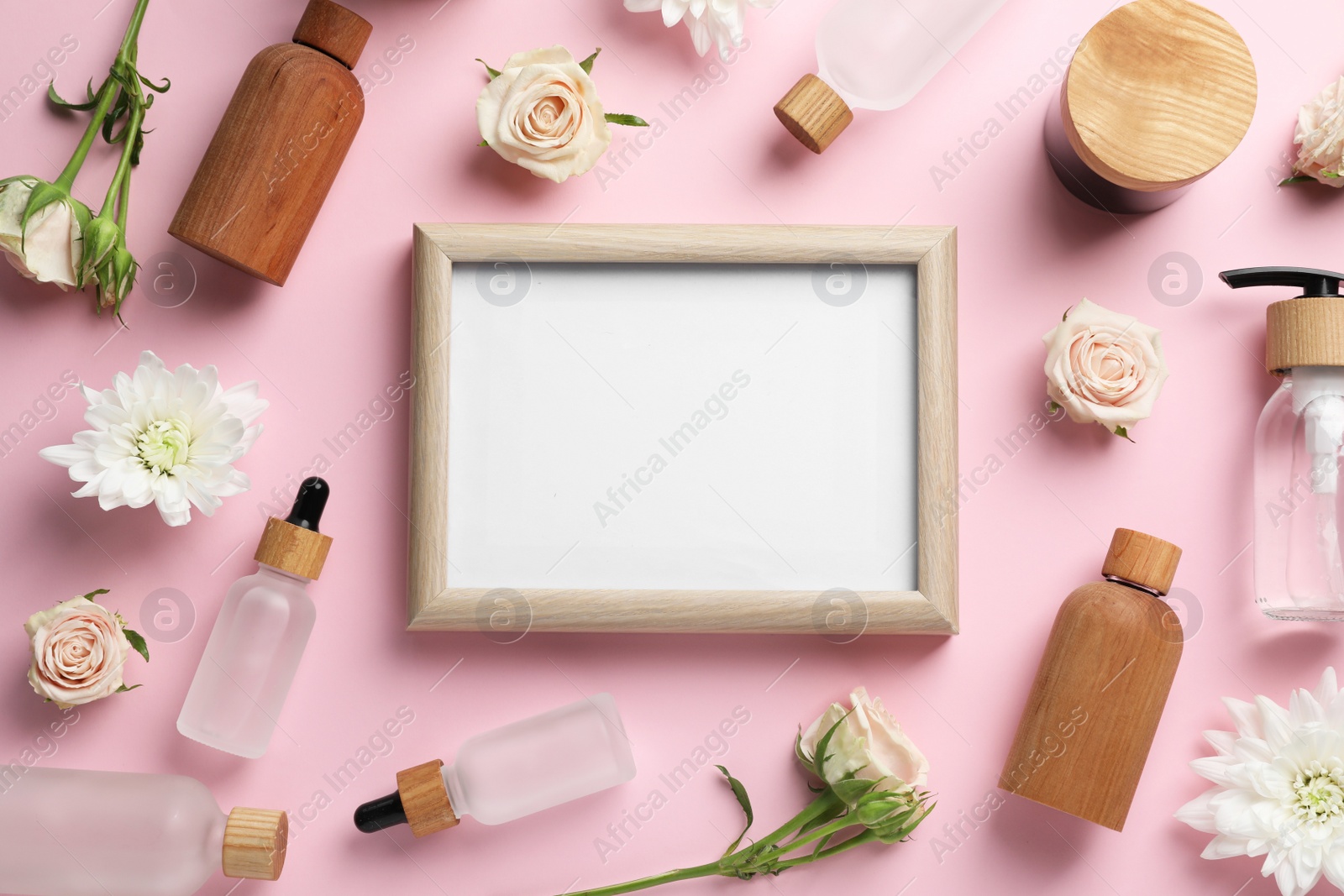 Photo of Blank white board with cosmetics and flowers on light pink background, flat lay. Space for text