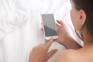 Photo of Young woman holding mobile phone with blank screen in hand on bed