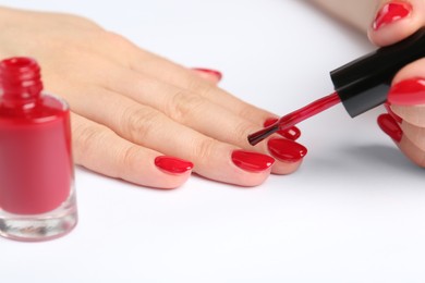 Photo of Woman painting nails with red polish on white background, closeup