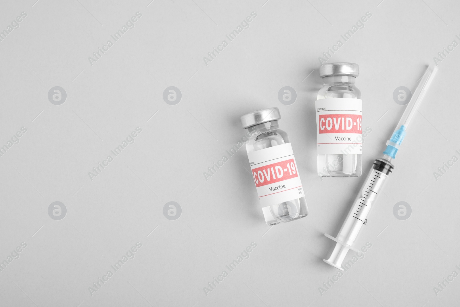 Photo of Vials with coronavirus vaccine and syringe on light background, flat lay. Space for text