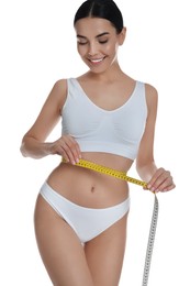 Young woman measuring waist with tape on white background